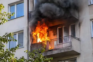 Flăcări mari și fum dens negru ies de pe un balcon al unei clădiri de apartamente.