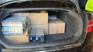În portbagajul unui autoturism negru sunt așezate cutii de carton și mai multe pachete de țigări grupate în cutii de plastic transparente.