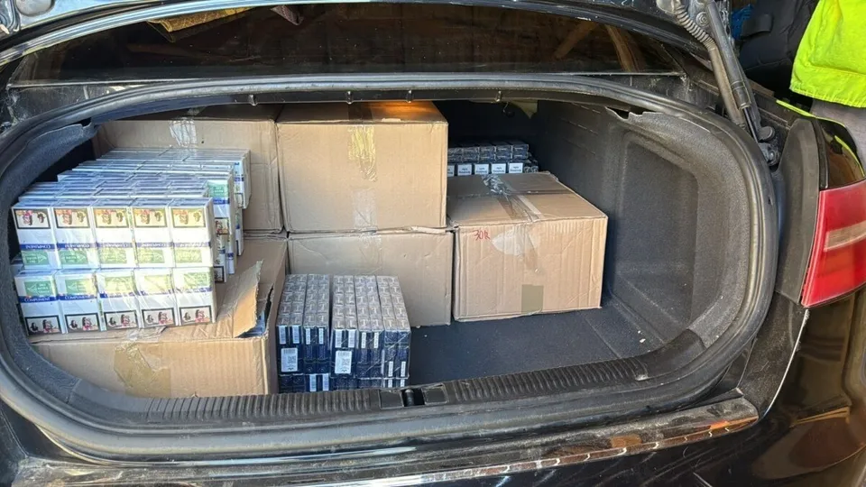 În portbagajul unui autoturism negru sunt așezate cutii de carton și mai multe pachete de țigări grupate în cutii de plastic transparente.