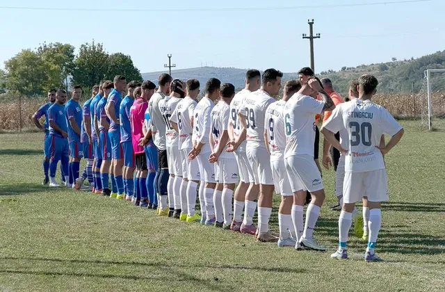 O linie de jucători de fotbal în echipamente albastre și albe stă întinsă pe un teren de iarbă sub un cer senin.