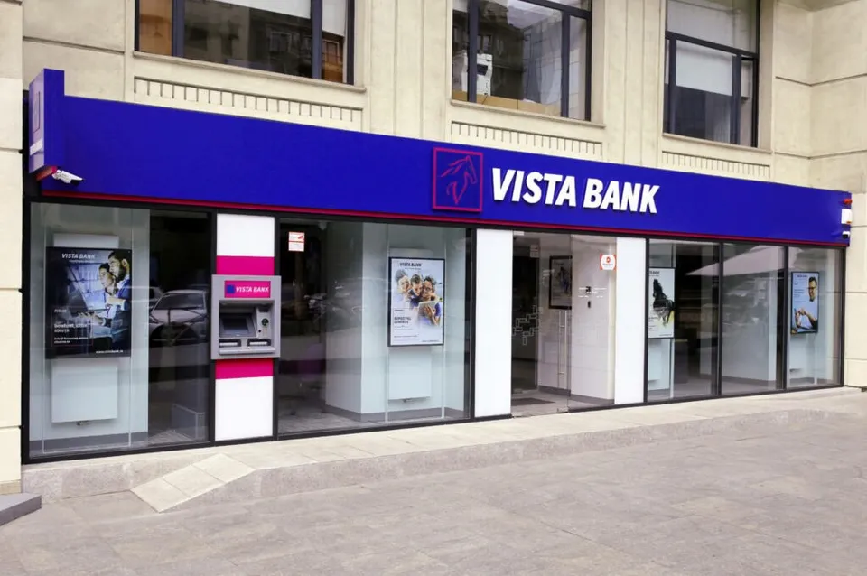 O sucursală Vista Bank cu vitrine mari de sticlă, un bancomat roz și alb și panouri publicitare afișate în interior.