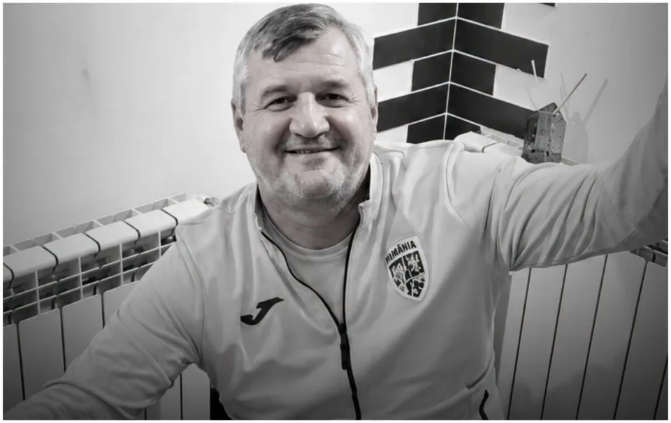 Un bărbat zâmbind poartă un hanorac alb cu un logo pe piept și un fermoar în față.