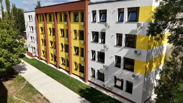O clădire modernă cu fațadă albă, galbenă și maro dispune de ferestre negre și unități de aer condiționat montate pe exteriorul pereților.