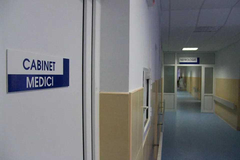 Un coridor interior are o ușă cu un panou „CABINET MEDICI”, pereți bicolori, balustradă metalică și o altă ușă în fundal.
