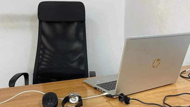 Un birou cu laptop deschis, scaun negru, mouse, ceas și cabluri pe blatul de lemn.