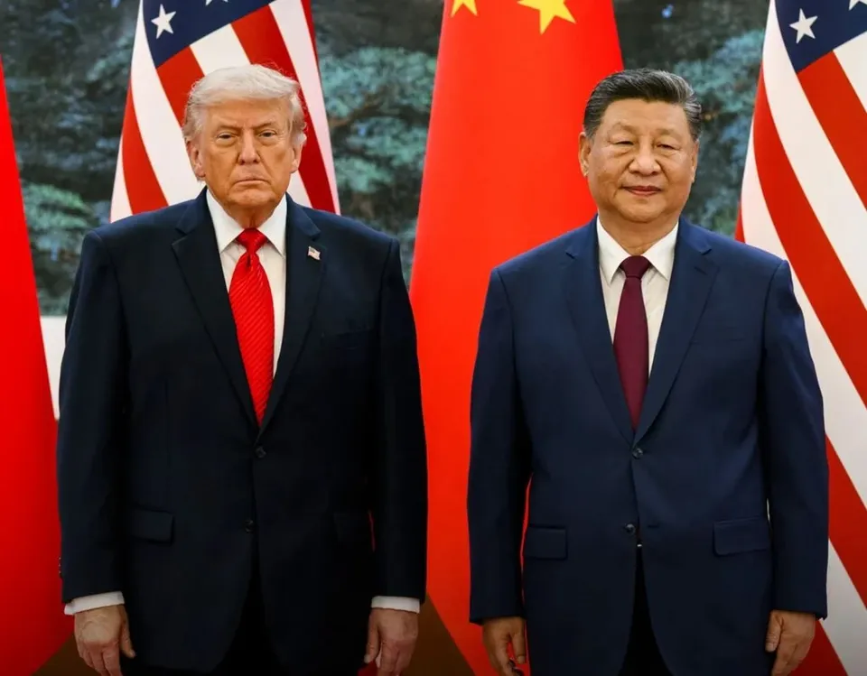 Un bărbat cu cravată roșie și un bărbat cu cravată purpurie stau în picioare în fața unor steaguri americane și chinezești.