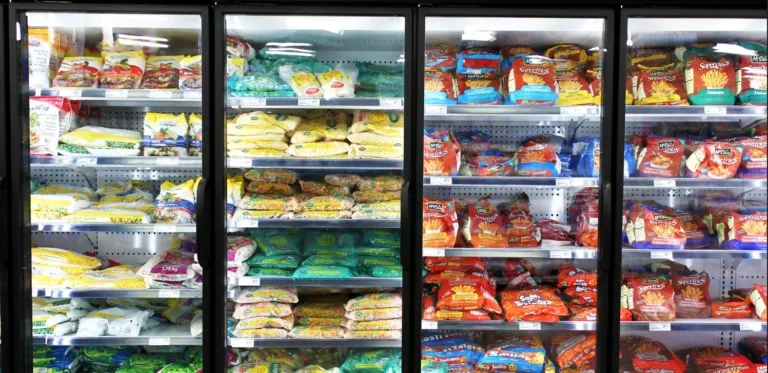 Rânduri de vitrine frigorifice cu uși de sticlă conținând diverse produse alimentare ambalate pe rafturi albe.