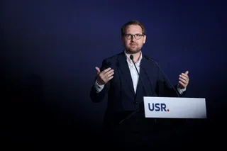 Un bărbat cu ochelari și costum închis stă în spatele unui podium alb pe care scrie USR.