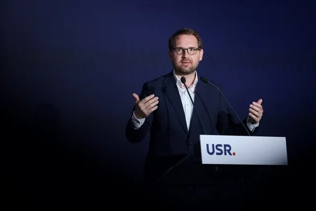 Un bărbat cu ochelari și costum închis stă în spatele unui podium alb pe care scrie USR.