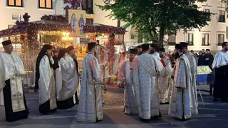Un grup de bărbați îmbrăcați în robe albe și decorate stau pe o stradă lângă un decor floral iluminat.