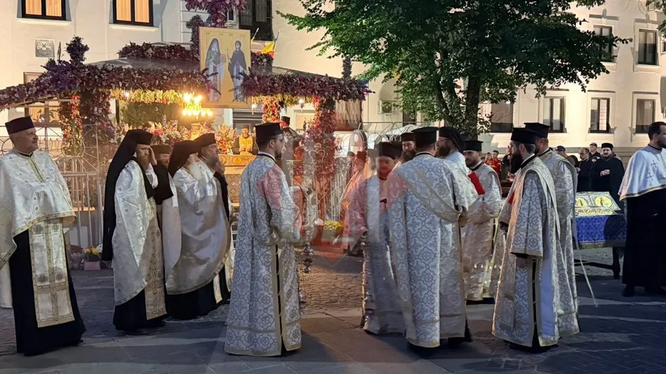 Un grup de bărbați îmbrăcați în robe albe și decorate stau pe o stradă lângă un decor floral iluminat.