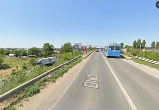 O autostradă cu două benzi de circulație, marcajele DN3 pe asfalt și un autobuz albastru circulând în depărtare sub un cer senin.