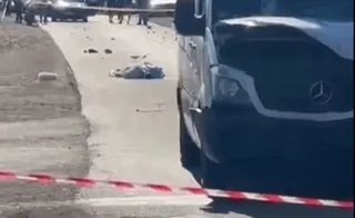 O autoutilitară albă este parcată pe marginea unui drum lângă o bandă de delimitare roșu și alb, având obiecte împrăștiate pe asfalt.