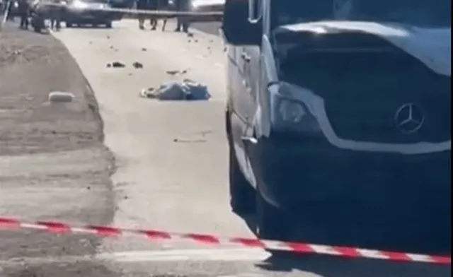 O autoutilitară albă este parcată pe marginea unui drum lângă o bandă de delimitare roșu și alb, având obiecte împrăștiate pe asfalt.