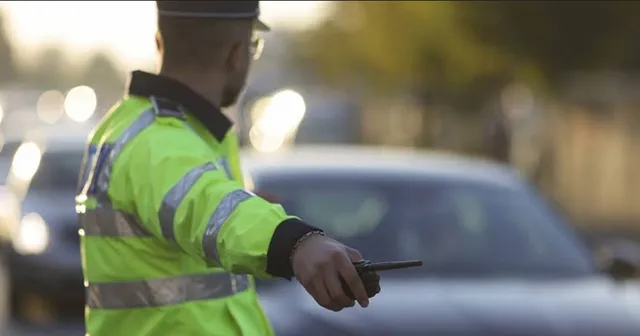 Un polițist în uniformă reflectorizantă, cu spatele la privitor, dirijează traficul, ținând o stație radio în mână.