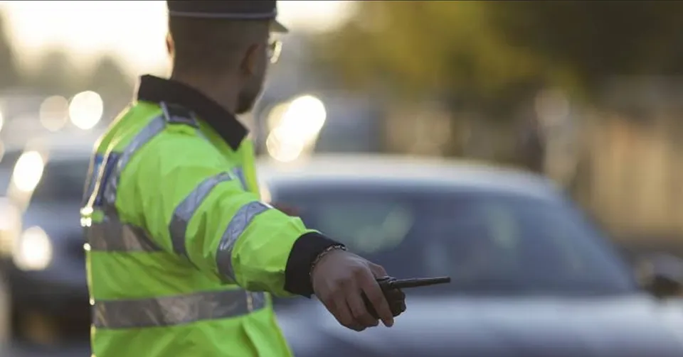 Un polițist în uniformă reflectorizantă, cu spatele la privitor, dirijează traficul, ținând o stație radio în mână.