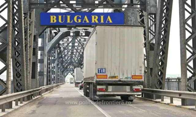 Un camion alb cu inscripția TIR circulă pe un pod metalic sub un panou albastru pe care scrie BULGARIA.