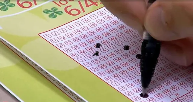 O mână ține un instrument de scris negru și marchează numere pe un bilet de loterie cu pătrățele numerotate pe un fundal galben.