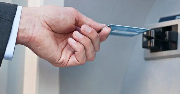 O mână ține un card bancar și îl introduce într-un aparat de tip ATM.