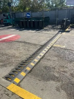 Un dispozitiv de tip bumper cu marcaje galbene este montat pe suprafața asfaltului lângă un bord curb marcat cu galben.