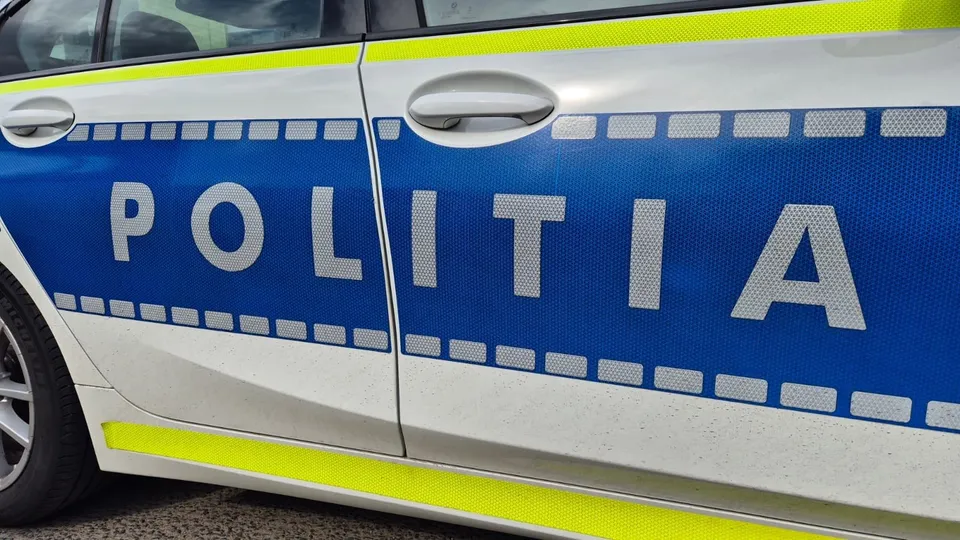 Un autovehicul alb cu banda albastră pe lateral pe care este scris textul POLITIA în litere mari și albe.