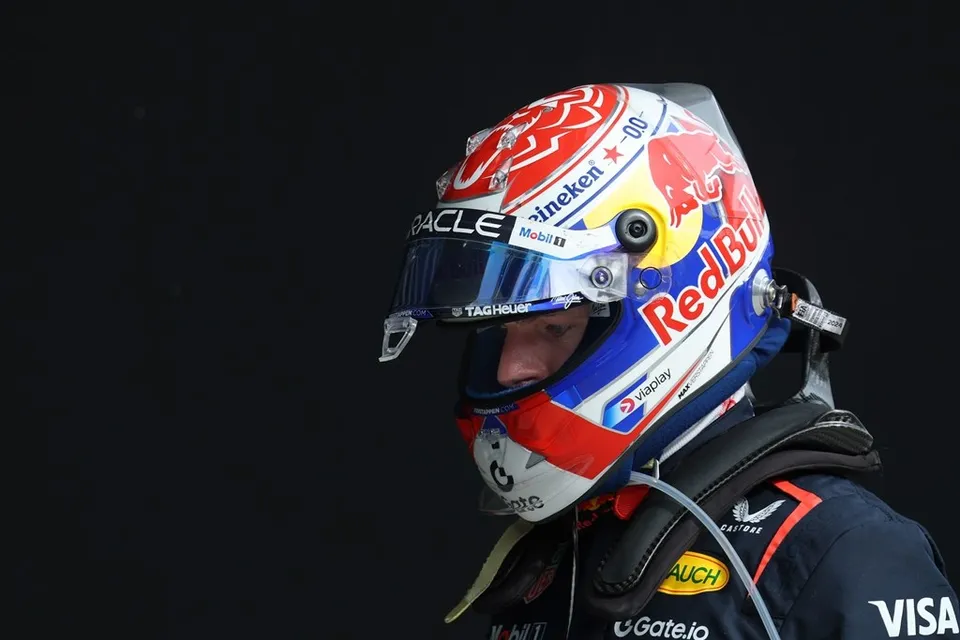 Un pilot poartă un cască de protecție colorată cu logourile Red Bull și Heineken, fiind vizibil cu o parte a feței sub vizieră.