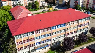 O vedere aeriană prezintă un clădire mare cu acoperiș roșu și numeroase ferestre dispuse în rânduri pe fațada de culoare deschisă.