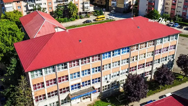 O vedere aeriană prezintă un clădire mare cu acoperiș roșu și numeroase ferestre dispuse în rânduri pe fațada de culoare deschisă.