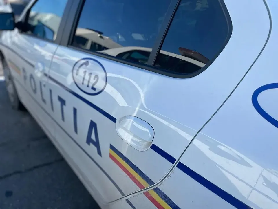 Un detaliu al unui autovehicul alb cu inscripția POLITIA și simbolul numărului de urgență 112 pe portiera din spate.