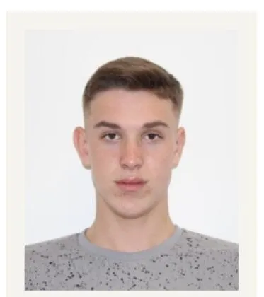 Un bărbat tânăr cu părul scurt și deschis la culoare poartă un tricou gri cu puncte negre pe un fundal alb.