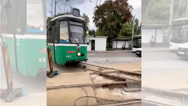 Un tramvai verde și alb circulă pe șine într-o zonă cu pavaj și vegetație sub un cer înnorat.
