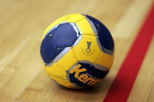 O minge de handbal galbenă și albastră cu inscripții negre se află pe un teren de lemn lângă o linie roșie.