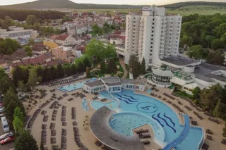 O vedere aeriană prezintă un complex hotelier cu o clădire înaltă albă și o piscină de forme neregulate în fața acesteia.