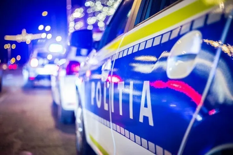Un autovehicul de poliție albastru și alb cu inscripția POLIȚIA este parcat pe un drum noaptea sub lumini strălucitoare.