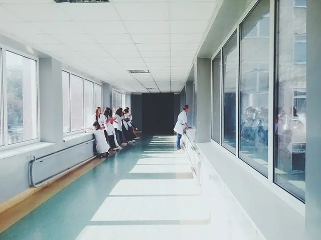 O grupă de persoane în halate albe stă pe un pervaz lângă ferestre, într-un coridor lung și luminos cu podea de culoare deschisă.