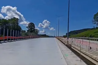 O porțiune de drum asfaltat cu bariere metalice pe margini, sub un cer albastru cu nori albi și vegetație verde în fundal.