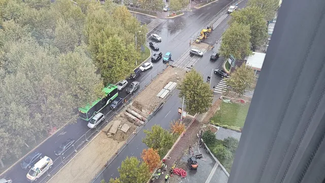 O vedere de sus asupra unui șantier de la marginea unei străzi cu mașini, un autobuz verde și unelte de construcție pe nisip.