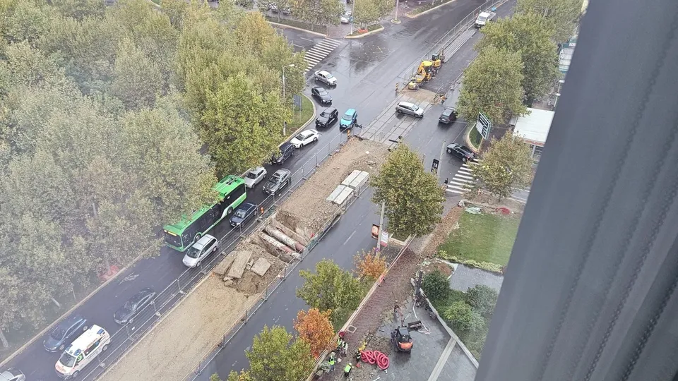 O vedere de sus asupra unui șantier de la marginea unei străzi cu mașini, un autobuz verde și unelte de construcție pe nisip.
