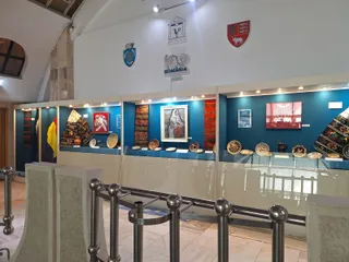 Obiecte de ceramică, textile și piese din lemn sunt expuse în vitrine pe un fundal albastru într-o încăpere cu pereți albi.