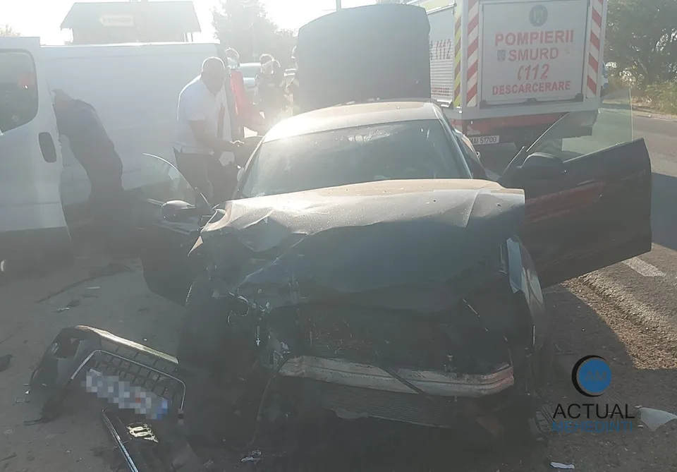 Un autoturism negru cu partea frontală zdrobită este situat pe drum, lângă un vehicul alb și o mașină neagră cu portiera deschisă.