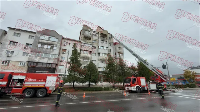 Pompierii lucrează lângă un camion roșu și o scară extensibilă în fața unui bloc de apartamente de culoare deschisă sub un cer gri.