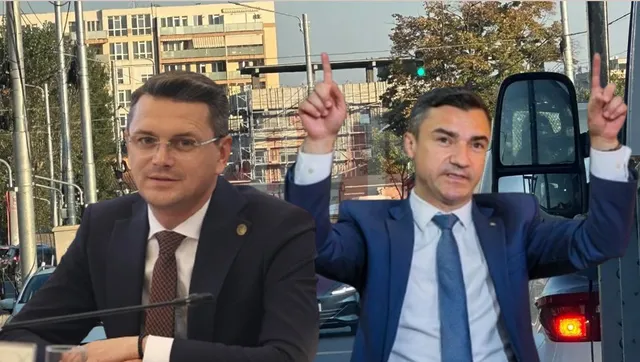 Un bărbat în costum albastru stă cu brațele ridicate și degetele arătând în sus, lângă un alt bărbat în costum închis.