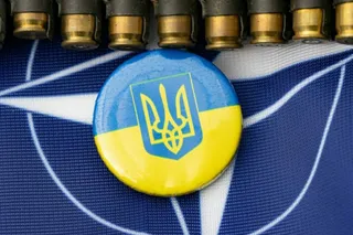 Un buton rotund cu culorile albastru și galben și un simbol de trident este așezat pe un material textil albastru cu linii albe.