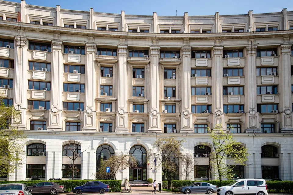 O clădire înaltă de culoare deschisă cu numeroase ferestre, balcoane și unități de aer condiționat dispuse pe mai multe etaje sub un cer senin.