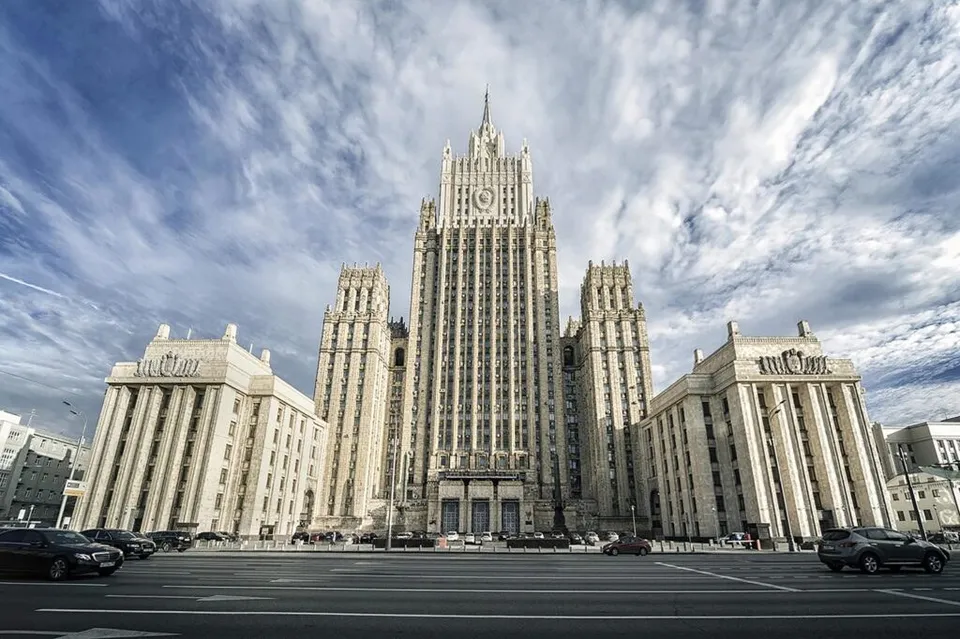 O clădire înaltă, de stil arhitectural monumental, cu multe ferestre, este situată pe o stradă largă cu mașini parcate în față sub un cer înnorat.