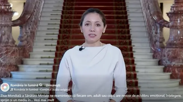 O femeie cu părul întunecat și o bluză albă stă în fața unei scări largi cu trepte de marmă și un covor roșu decorat.