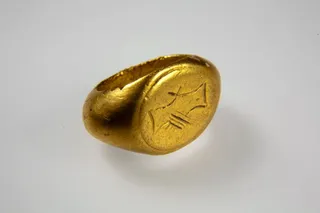 Un inel de aur cu o suprafață elipsoidală și un desen gravat este așezat pe un fundal gri deschis.