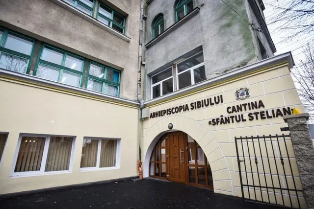O clădire cu ferestre verzi și o porțișcă arcuită pe care scrie Arhiepiscopia Sibiuului și Cantina Sfântul Stelian.