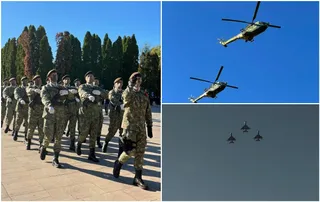 Soldați în uniforme de camuflaj merg pe o platformă pavată, în timp ce două elicoptere și trei avioane zboară pe un cer senin.