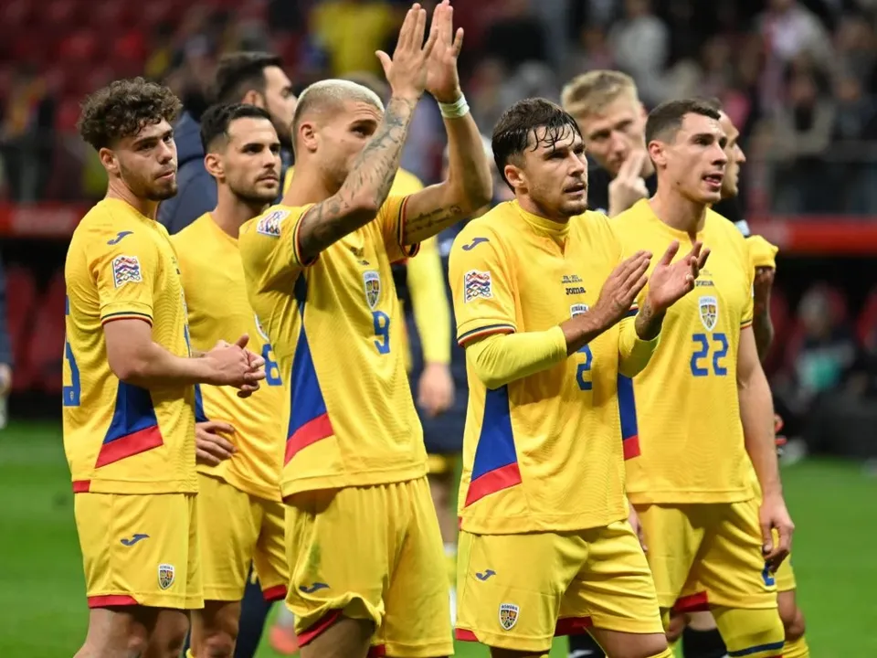Câțiva jucători de fotbal îmbrăcați în echipamente galbene stau pe terenul de fotbal sub privirea spectatorilor din tribune.
